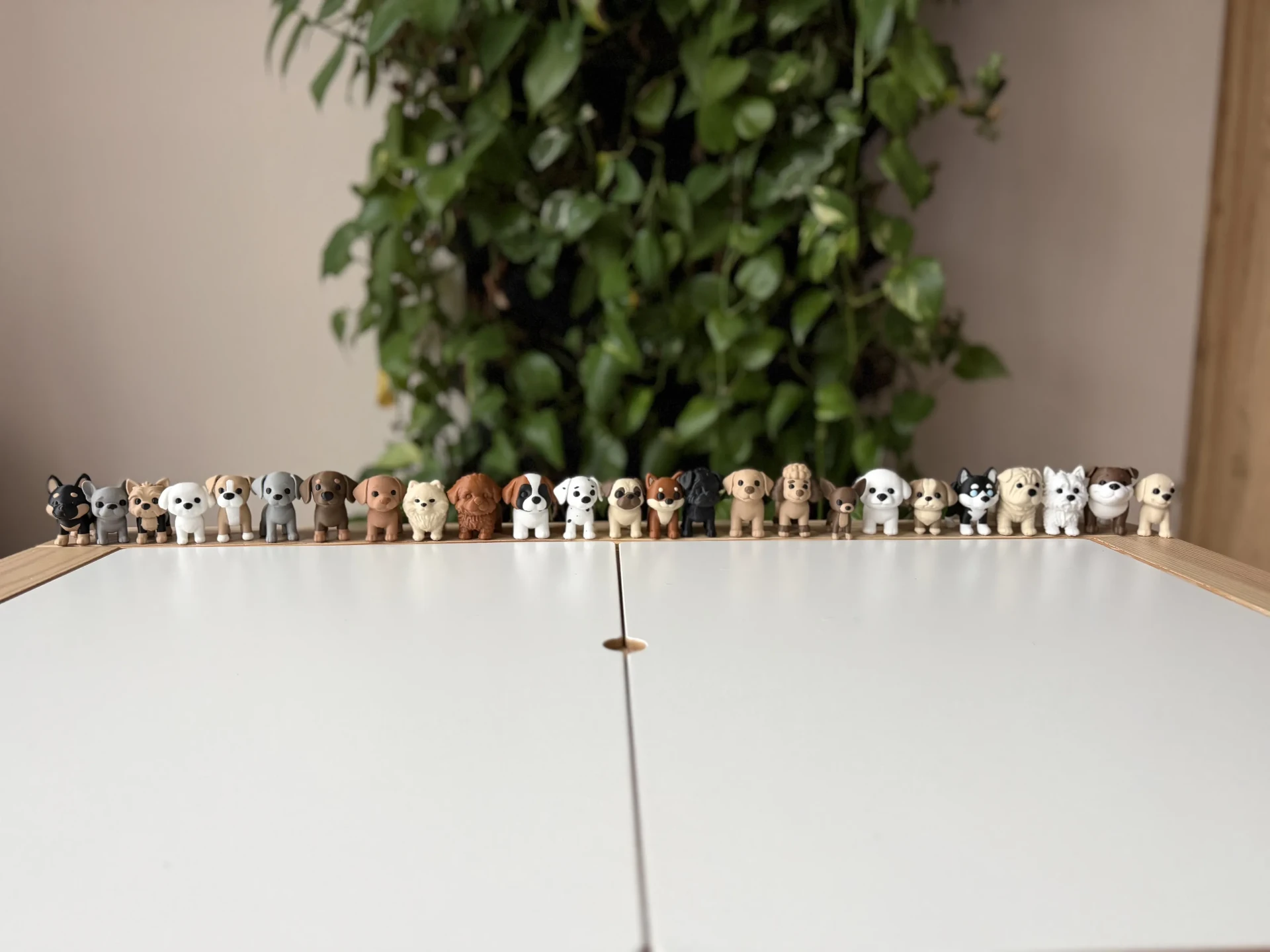 A long row of small 3D printed dog figurines of many different breeds on a wooden shelf